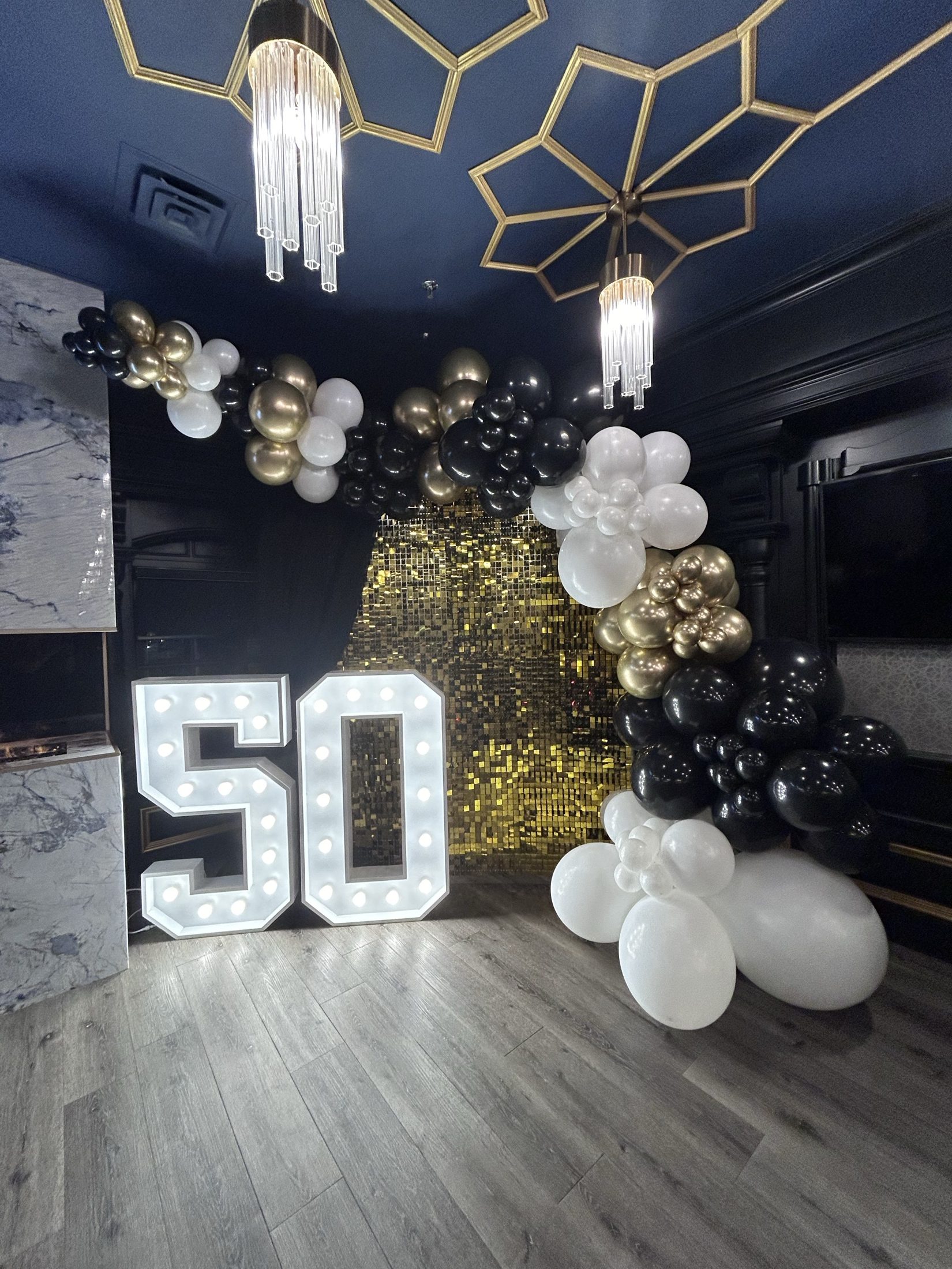A fiftieth birthday wall with gold marquee numbers and white balloon columns