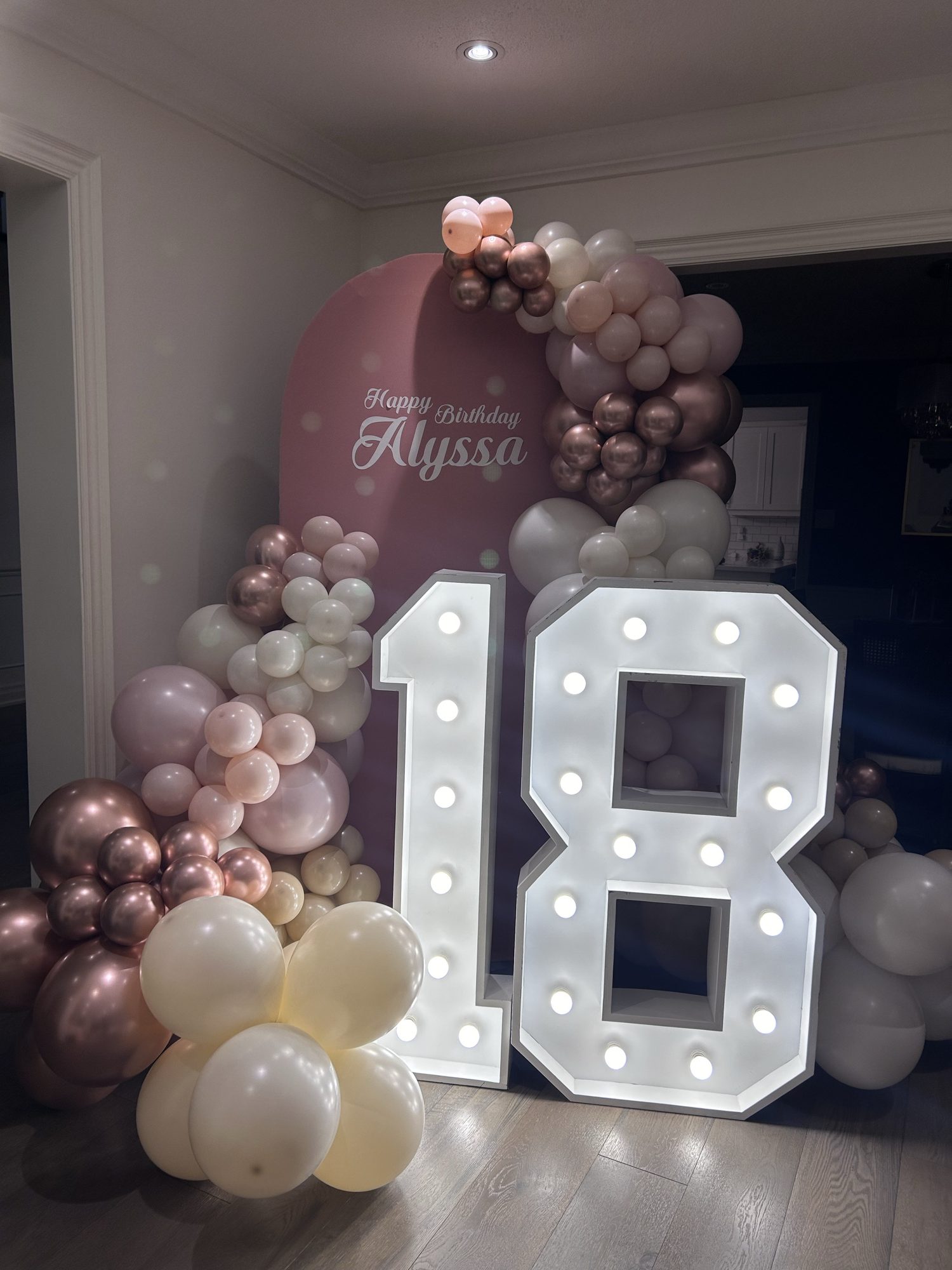An eightieth birthday backdrop with lit marquee numbers and a mauve balloon garland