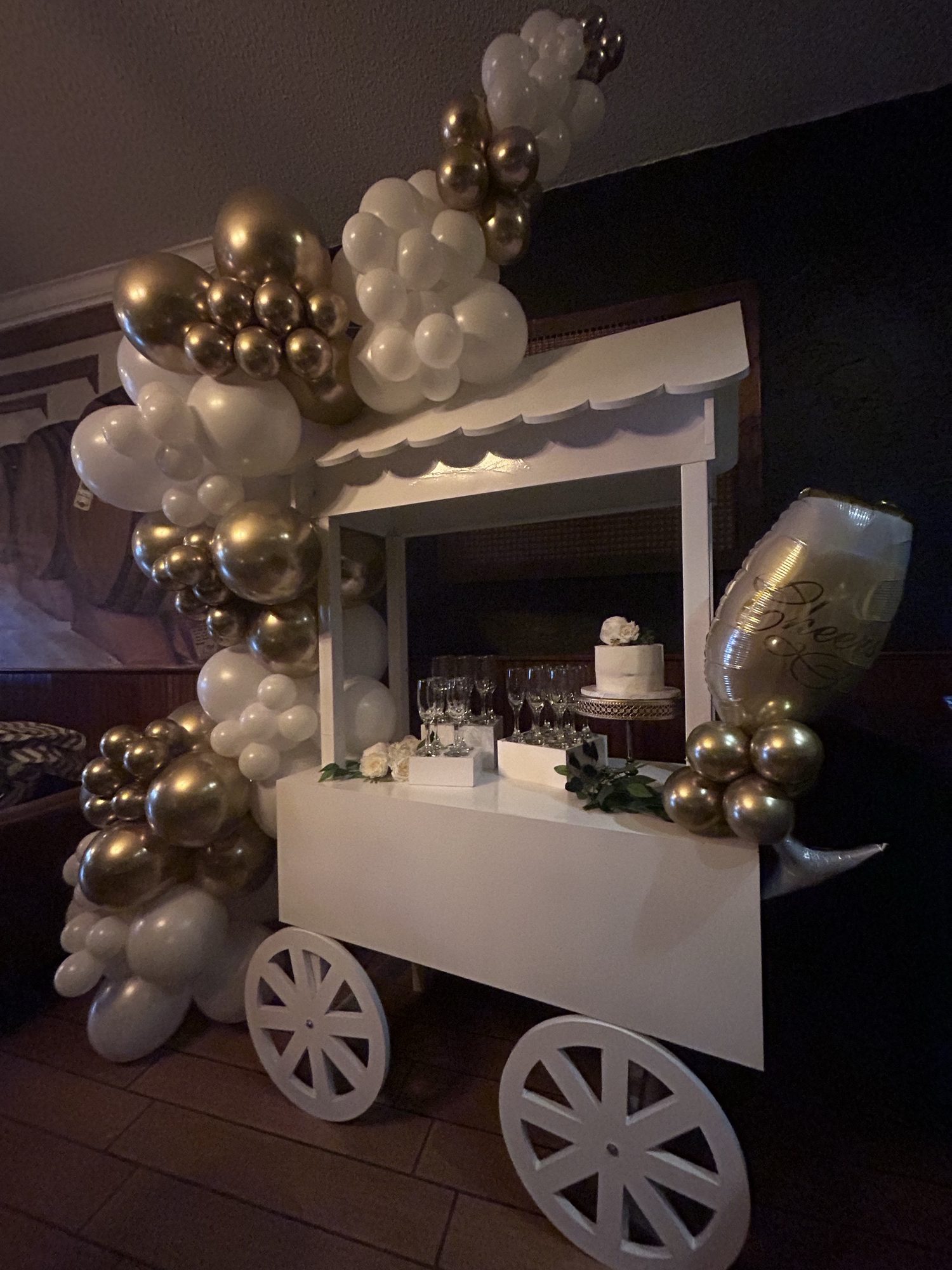 A white carriage backdrop lit by gold and cream balloon clouds